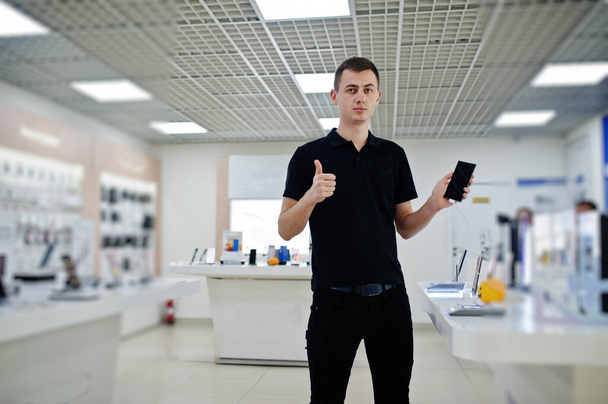 Seller man mobile phone professional consultant in tech store or shop hold new smartphone at  hand and show thumb up. - Фото, изображение