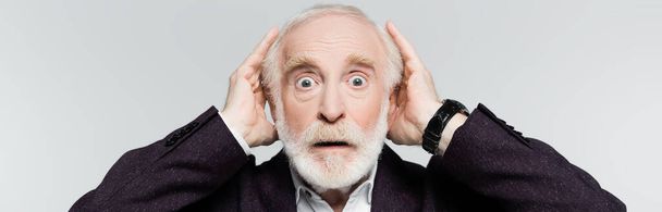 Hombre mayor sorprendido con las manos cerca de la cabeza mirando la cámara aislada en gris, pancarta - Foto, Imagen