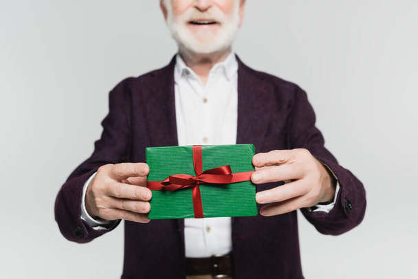 Gesneden weergave van geschenkdoos in handen van lachende oudere man op wazige achtergrond geïsoleerd op grijs  - Foto, afbeelding