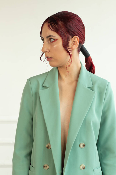 portret młodej dziewczyny z rudymi włosami z makijażem i w zielonej kurtce i jtns w studio, moda piękna - Zdjęcie, obraz