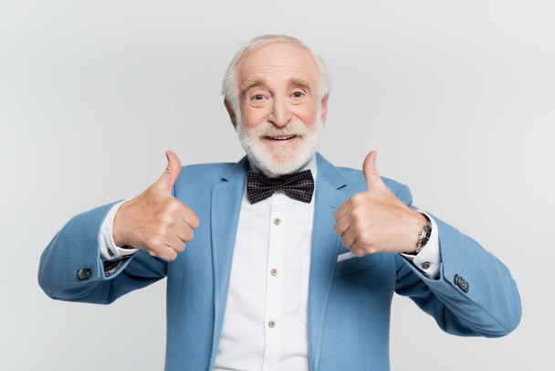 Sorrindo homem idoso de jaqueta e gravata arco mostrando como isolado no cinza  - Foto, Imagem