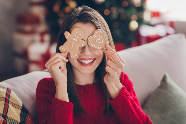 Portrait of positive girl cover eyes with x-mas heart man shape ginger bread cookie toothy smile in house indoors - Foto, imagen