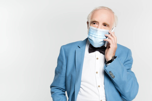 Senior man in medical mask talking on smartphone isolated on grey  - 写真・画像