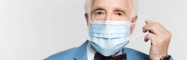 Elderly man holding medical mask isolated on grey, banner  - 写真・画像