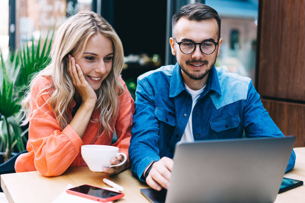 Positiivinen valkoihoinen mies ja nainen katsomassa videota kannettavan tietokoneen yhteistyössä projektissa, 20s hymyilevä hipster kaverit etsivät tietoa ja selailu web-sivun varaus kahvila terassi - Valokuva, kuva