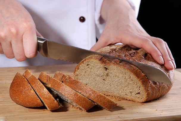 Cutting bread on wooden board on dark background - 写真・画像