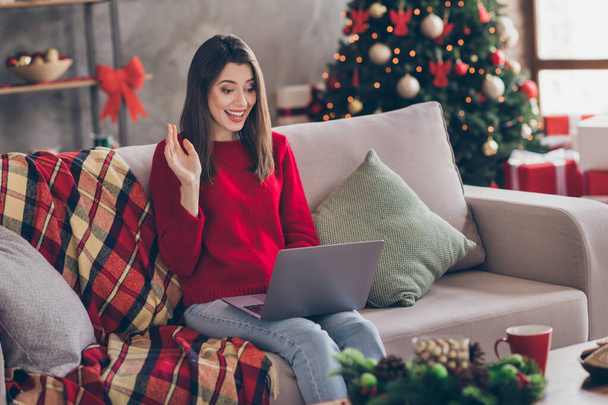 Photo of young lovely lady sit sofa hold netbook waving hand wear red sweater jeans in decorated living room home indoors - Φωτογραφία, εικόνα