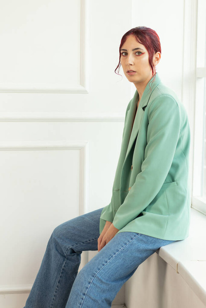 portrait of a young girl with red hair with makeup and in a green jacket and jtns in the studio, beauty fashion - 写真・画像