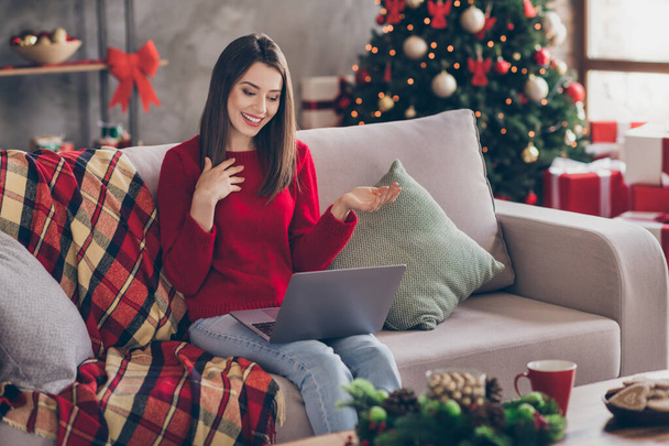 Photo of young cute lady sit sofa hold computer arm chest toothy smile wear red sweater jeans in decorated x-mas living room home indoors - Zdjęcie, obraz