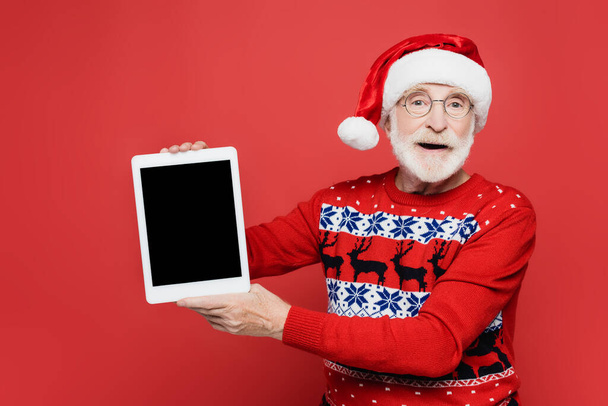 Senior férfi télapó kalap kezében digitális tabletta üres képernyő elszigetelt piros - Fotó, kép