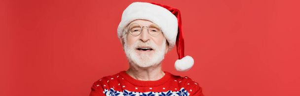 Homme âgé joyeux en lunettes et chapeau de Père Noël isolé sur rouge, bannière  - Photo, image