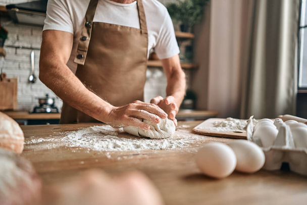 Cropped photo of mature male chef baking bread or delicious bun on the kitchen. Baking concept - Fotoğraf, Görsel
