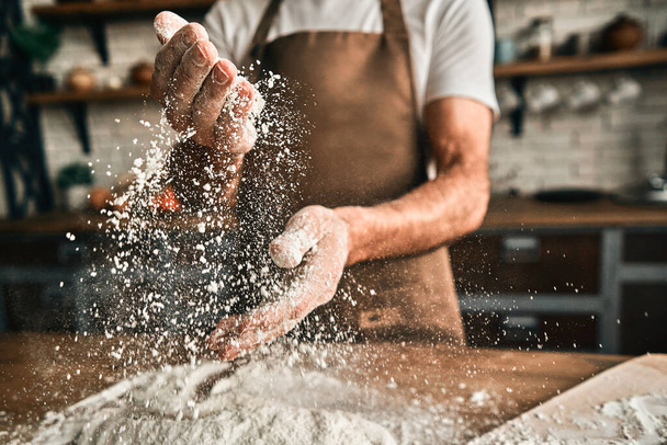 Cropped photo of male chef preparing meal and using flour while standing on the kitchen at home. Baking process concept - Fotografie, Obrázek