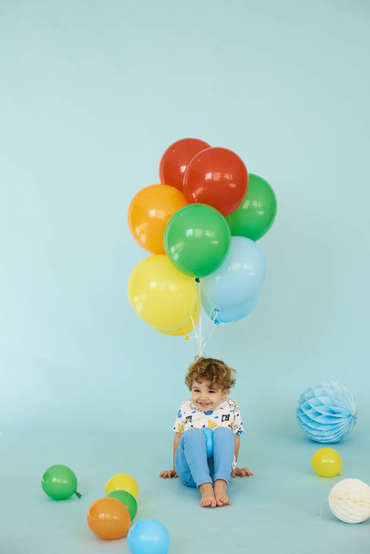 Full length portrait of cheerful boy holding balons posing against blue background - Foto, afbeelding