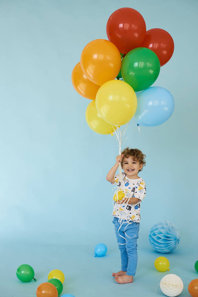 Full length portrait of cheerful boy holding balons posing against blue background - Fotó, kép