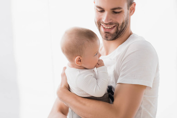 fröhlicher Vater hält kleinen Jungen im Arm, der Finger lutscht  - Foto, Bild