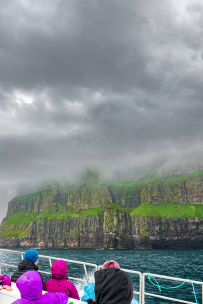 Неузнаваемые туристы на лодке наблюдают впечатляющие Вестманнские скалы - Фото, изображение
