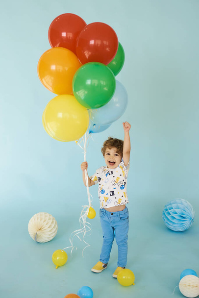 Full length portrait of cheerful boy holding balons posing against blue background - Photo, image