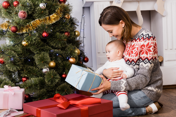 hymyilevä nainen tilalla läsnä lähellä vauva poika ja koristeltu joulukuusi - Valokuva, kuva