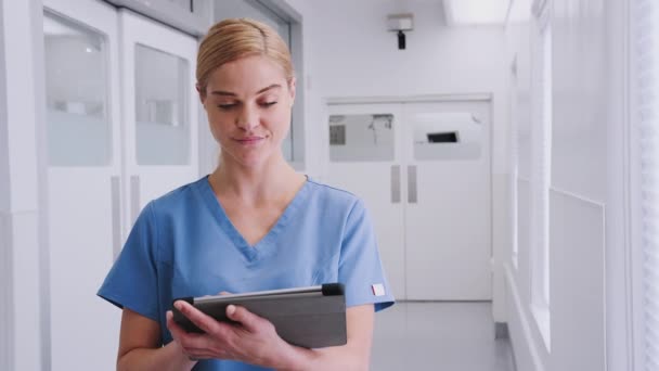 Portrait of smiling female doctor wearing scrubs using digital tablet in hospital corridor - shot in slow motion - Filmati, video
