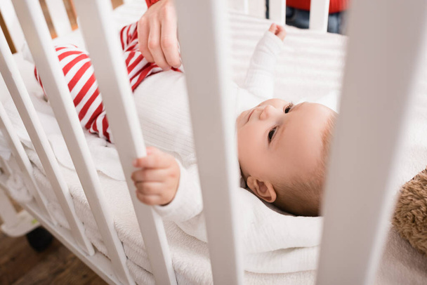 hand of father near infant son in baby crib on blurred foreground  - Φωτογραφία, εικόνα