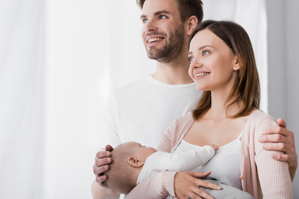 smiling woman holding in arms infant boy near cheerful husband  - Foto, Bild