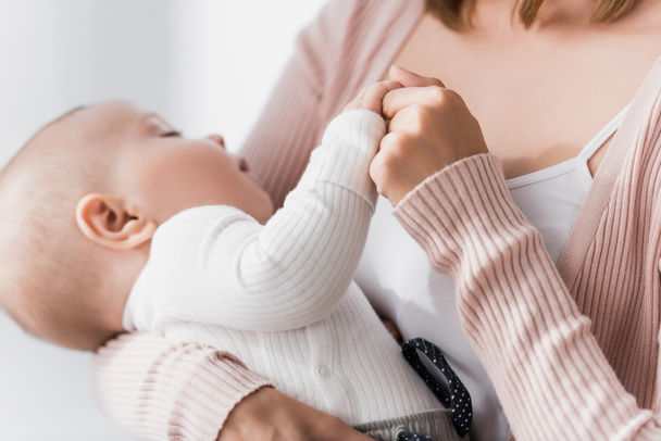 zblízka pečující žena drží ruce s kojeneckým chlapcem na rozmazaném pozadí  - Fotografie, Obrázek