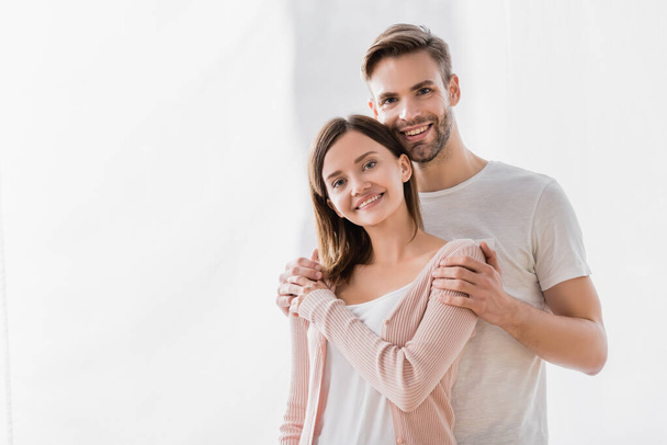 happy man embracing cheerful wife and looking at camera - Foto, Bild