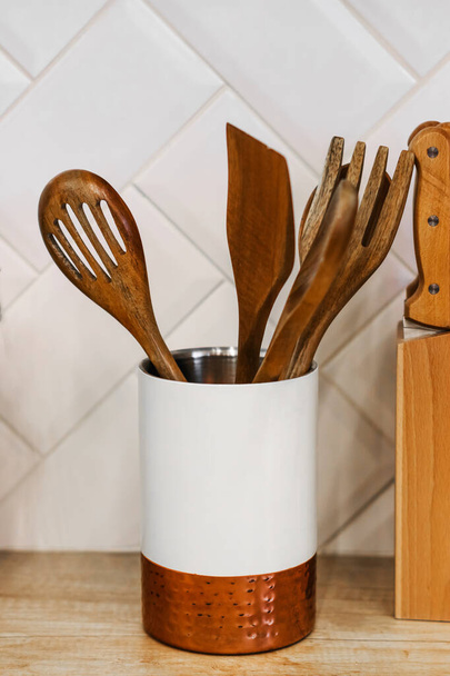 kitchen utensils for cooking are on the countertop in the kitchen. wooden spoons, scoops in a glass stand. Scandinavian style in the interior of the kitchen - Фото, изображение
