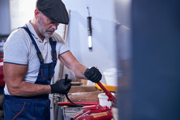 Bearded male mechanic in cap working in garage - Photo, Image