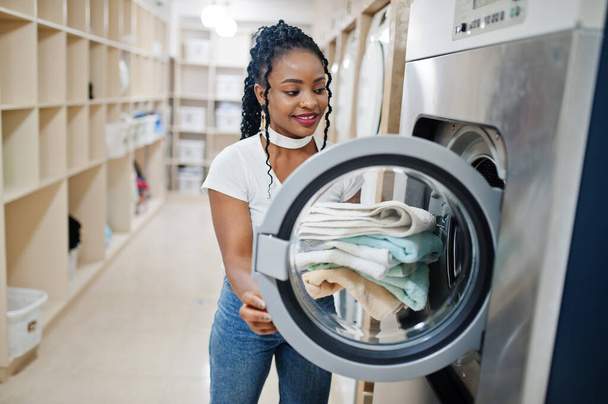 Cheerful african american woman with towels in hands near washing machine in the self-service laundry. - Foto, Bild
