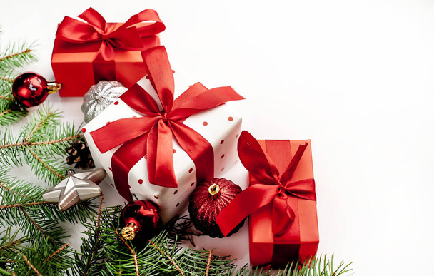 Composición navideña sobre fondo blanco con cajas de regalo blancas con cinta roja con ramas de abeto, juguetes. Ver arriba con espacio de copia para sus felicitaciones - Foto, Imagen