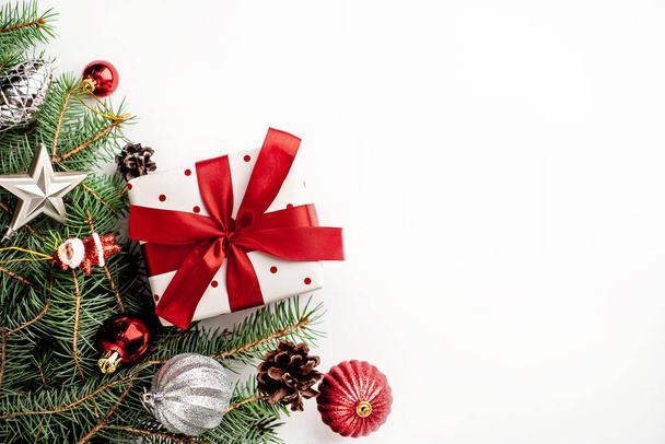 Weihnachtskomposition auf weißem Hintergrund mit weißer Geschenkschachtel mit rotem Band mit Tannenzweigen, Spielzeug. Ansicht oben mit Kopierraum für Ihre Glückwünsche - Foto, Bild
