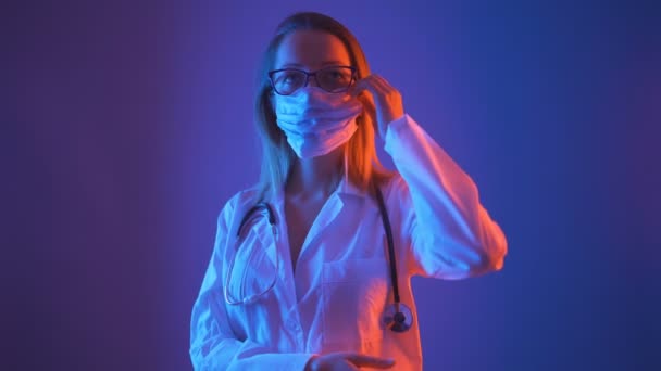 Красивая женщина-врач в очках и белом халате снимает медицинскую маску с лица - Кадры, видео