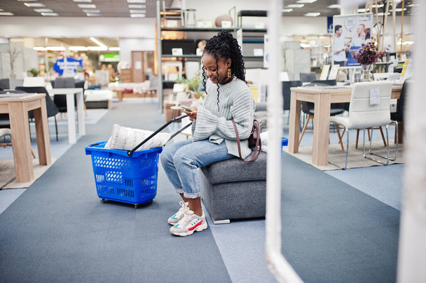 African woman with mobile phone and shopping basket in a modern home furnishings store. - Zdjęcie, obraz