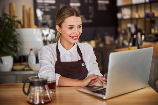 Saleswoman working at the laptop in coffee shop - Photo, Image