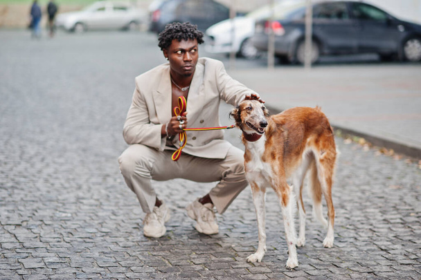 Stylish afro man in beige old school suit with Russian Borzoi dog. Fashionable young African male in casual jacket on bare torso. - Fotoğraf, Görsel