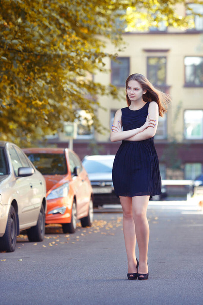 Portrait of a beautiful young girl in a little black dress on a summer day on a city street. - 写真・画像