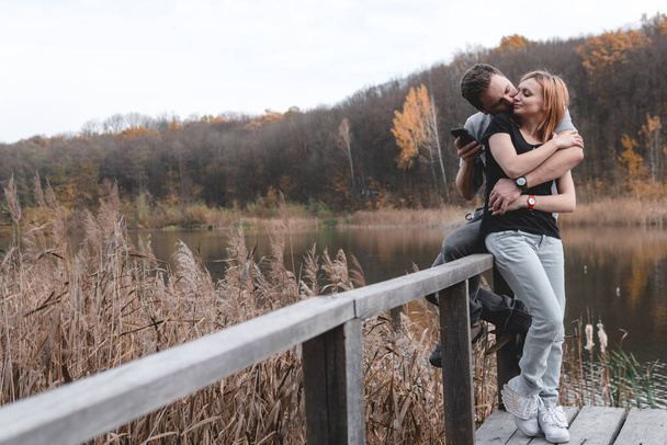 A couple on the old wooden bridge at a lake on autumn day in park. Forest on background. Happy togather, copy space for text. romantic moment, relationship. travel, hiking, outdoor. comfort - Photo, Image