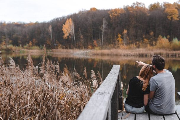 Una pareja en el viejo puente de madera en un lago en el día de otoño en el parque. Bosque en el fondo. Enfoque selectivo, copia espacio para texto. momento romántico, relación. viajes, senderismo, al aire libre. comodidad - Foto, imagen