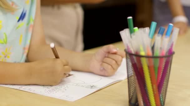 Крупним планом маленька мила дівчинка з кісками сидить за столом малює розмальовки
 - Кадри, відео