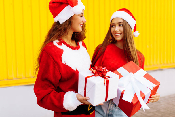 Celebrating Christmas. Happy friends in Santa Claus hats, with Christmas gifts - Fotografie, Obrázek