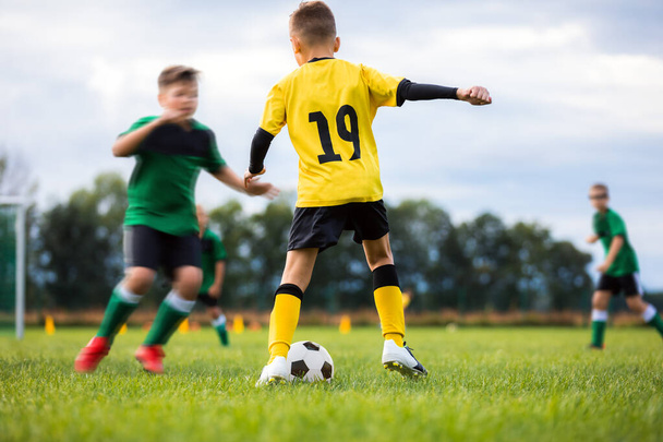 Jalkapalloseurojen pojat kilpailevat ulkoturnausottelussa. Jalkapallopeli koululaisille. Lapset yllään jalkapallo pelipaita urheiluvaatteet käynnissä ruohokentällä ja potkiminen jalkapallo pallo. Juniorijalkapallopeli - Valokuva, kuva