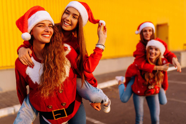group of happy friends wearing santa claus hats have fun and ride each other in the fresh air against a yellow wall - Foto, Imagem