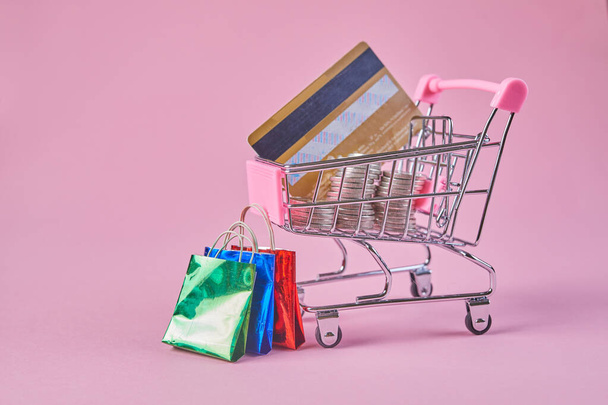 Shopping trolley with credit card on a pink background. Colorful paper shopping bags as creative idea for shopping online. - Foto, Bild