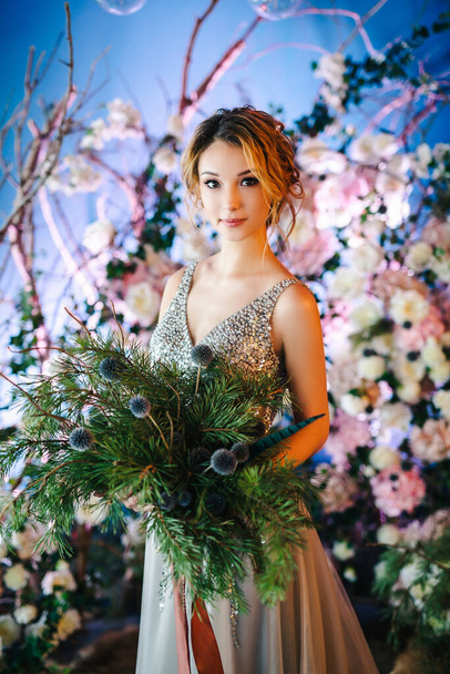 The bride in a wedding silver dress poses against a blue wall with decor. Winter wedding concept. Selected focus. Blurred background - Foto, Imagen