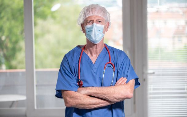 Portrait of senior surgeon with arms crossed wearing a face mask - Foto, imagen