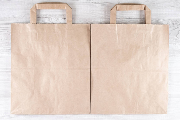 twee bruine ecologische papieren zak op een witte houten tafel. Plaats voor uw logo. - Foto, afbeelding