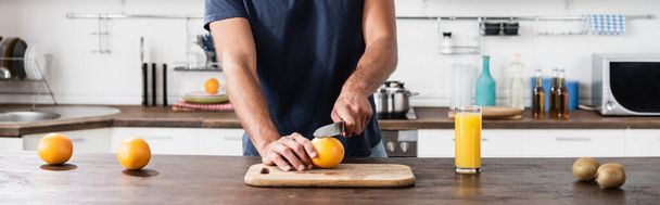 Viljelty näkymä mies leikkaa tuoretta appelsiinia lähellä kiiviä ja lasi appelsiinimehua, banneri  - Valokuva, kuva