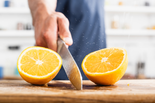 Close up view of halves of juicy orange and wet knife in hand of man on blurred background  - Foto, immagini
